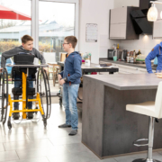 Kind im Stehtrainer todd und in Interaktion mit Kind auf Augenhöhe.