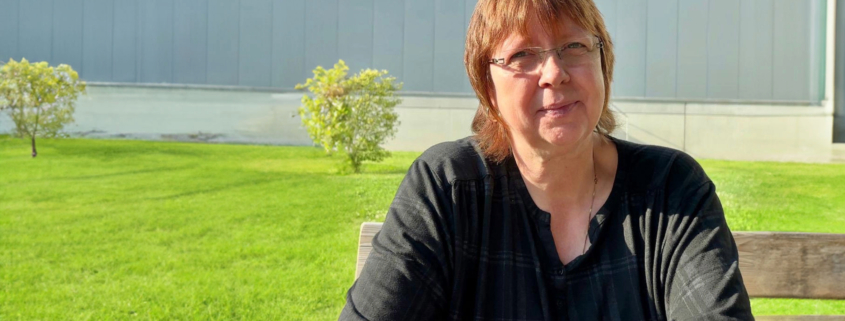 Sigrid Hirte, Teamleiterin der Polsterei und Näherei bei Schuchmann sitzt draußen am Tisch vor einer Rasenfläche