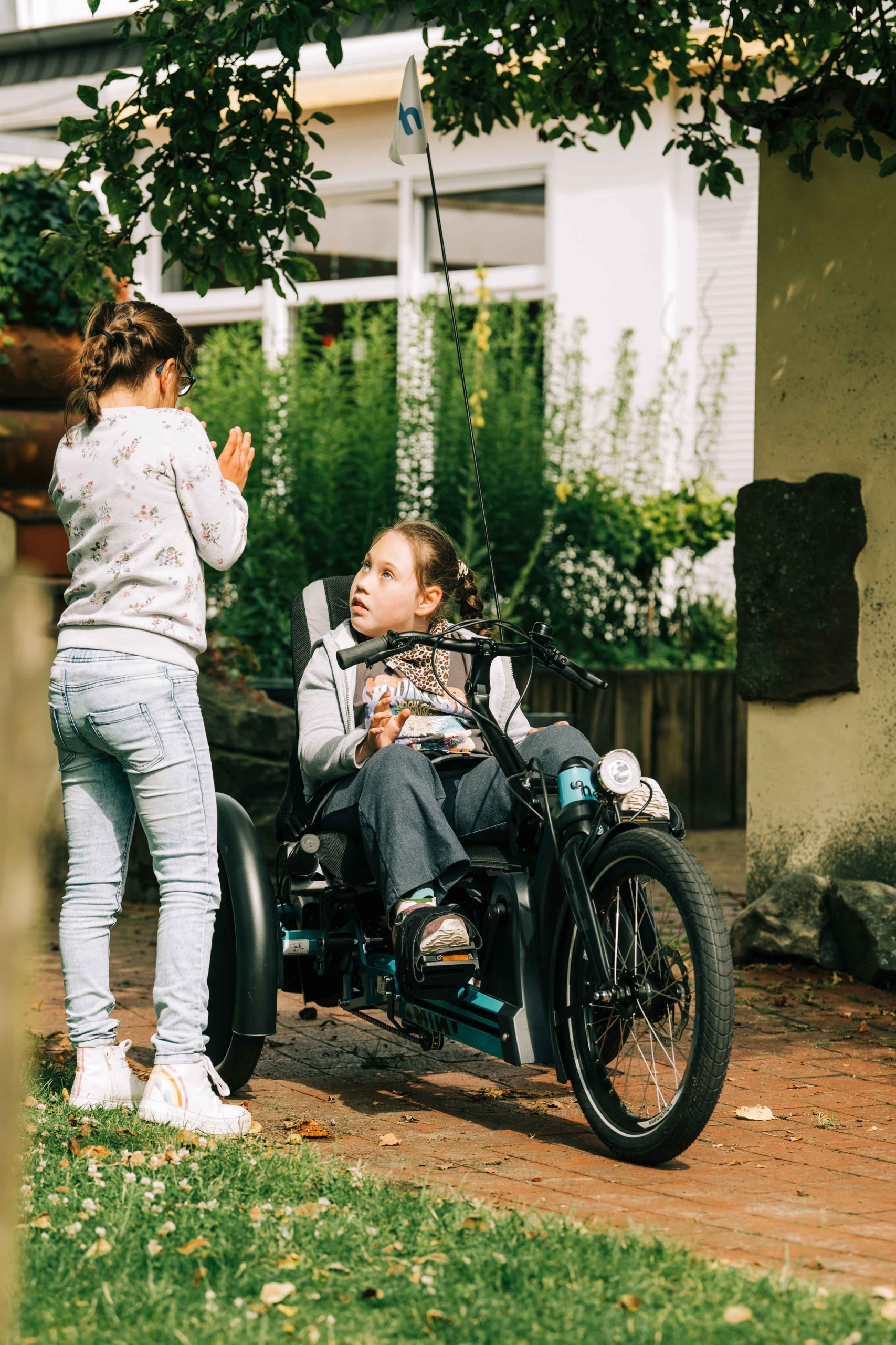 Junges Mädchen auf dem mats Liegedreirad der Firma Schuchmann. In Interaktion mit einem Mädchen, dass neben dem Rad steht.