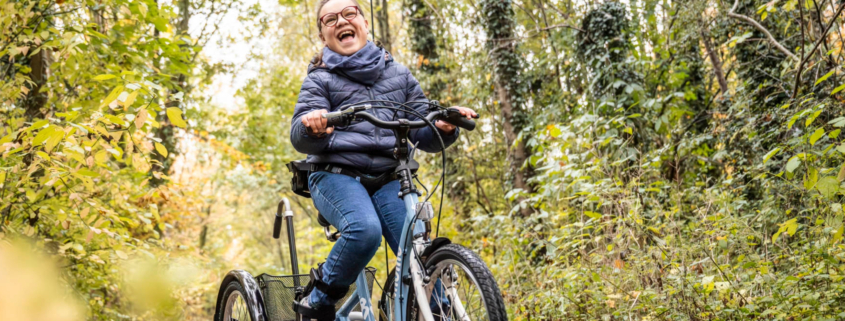 Ein Mädchen mit Behinderung sitzt auf dem momo dreirad. Einem Fahrrad für Kinder mit Behinderung.