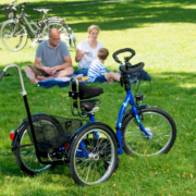 Dreirad von Schuchmann im Vordergrund. Im Hintergrund picknickt eine Familie mit Kind mit Behinderung.